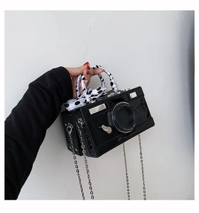 Detailed close-up of a camera-shaped handbag with silk scarf handle and metal chain