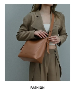 Brown leather bucket bag with adjustable strap worn by a model in a beige suit