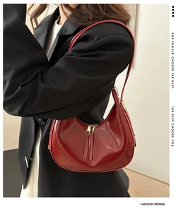 Detail of red glossy patent leather crescent shoulder bag with metallic dual zippers