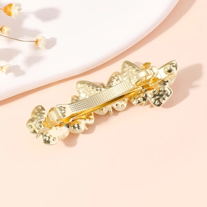 Golden alloy butterfly hair clip with rhinestones shown on a soft pink and white background