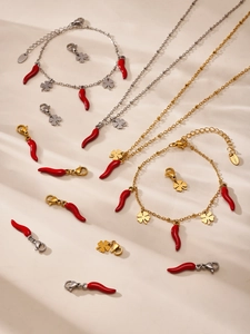 Detailed view of red chili and clover charms on gold stainless steel jewelry set