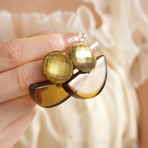 Handheld view of geometric resin drop earrings with gold glitter and amber charms
