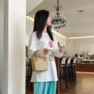 Detail of a woven straw handbag with brown leather handles held by a model in casual attire