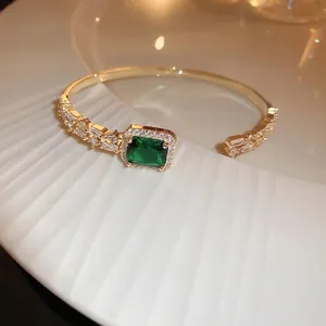 Elegant gold open bangle with emerald-green square zircon and white crystal accents