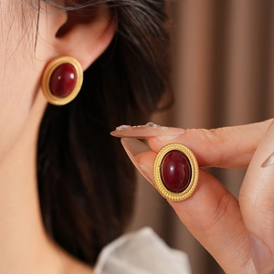 Close-up of vintage golden oval gemstone earrings with wine red stones worn by a model
