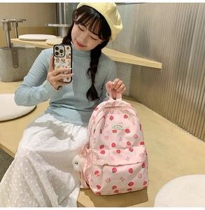 Detailed close-up of cute pink strawberry backpack with plush ball charm and heart prints