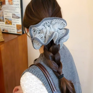 Detail of grey knitted flower hair scrunchie shown on a thick braided hairstyle