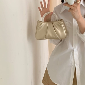 Detail of golden pleated cloud bag featuring premium pearl handle and metallic PU texture