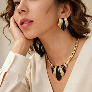Detail view of a gold metallic necklace and earring set with black enamel drops