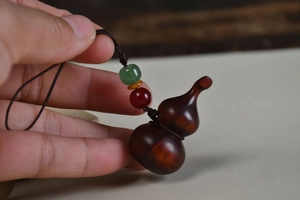 Close-up of a carved rosewood gourd pendant with colorful beads and dark woven cord