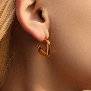 Close-up of a high-polished gold heart-shaped earring worn on a model ear