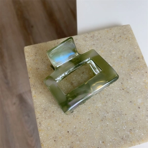 Macro detail of a green marble pattern acetate hair claw clip on a stone surface