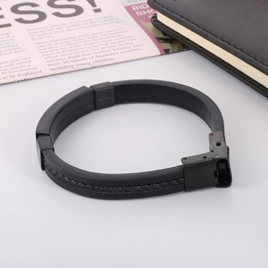 Detail of black leather braided bracelet with frosted metal clasp on a minimalist desk