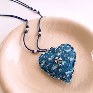 Collier cœur en denim bleu avec pendentif croix argentée sur plateau à bijoux beige