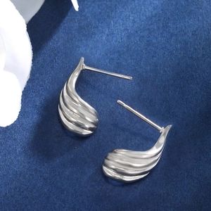 Macro detail of silver teardrop earrings with vertical grooved texture on blue background