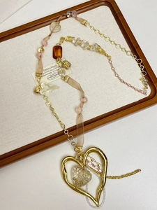 Detailed macro shot of a vintage gold hollow heart pendant and mixed material long chain