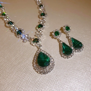Detailed close-up of emerald green teardrop necklace and earrings with silver pavé setting