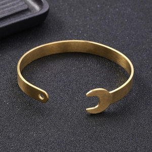 Macro detail of gold stainless steel wrench-shaped open bangle on a dark surface