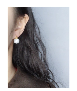 Close-up of a white pearl drop earring with gold hook worn by a female model