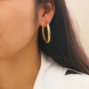 Detailed view of gold woven textured hoop earrings on model with retro polished finish