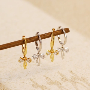 Macro shot of silver and gold bow earrings with sparkling crystal accents on wooden stand
