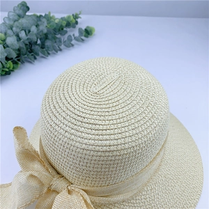 Gros plan d'un chapeau de soleil en paille beige avec tissage en spirale et grand nœud