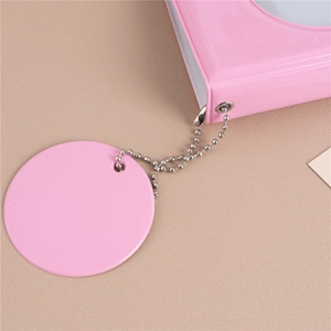 Pink photo album detail with a round tag and silver metal ball chain on beige surface