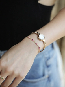 Dettaglio di un sottile bracciale d'oro con pietre rosa rettangolari e orologio dorato