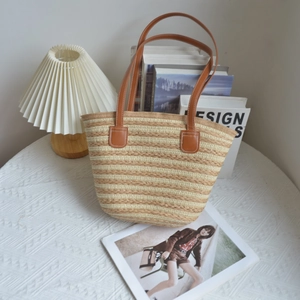 Detail of hand-woven straw tote bag with striped texture and brown leather straps