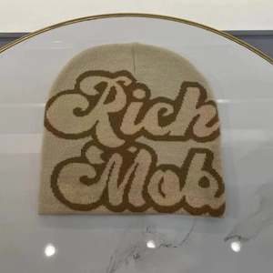 Close-up of beige knitted beanie featuring brown Rich Mob lettering on marble background