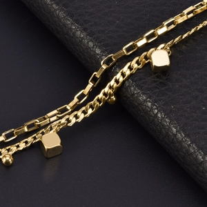 Macro detail of gold stainless steel link chains with square and bead charms on black leather