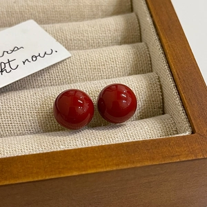 Close-up of glossy red spherical pearl earrings set against a soft beige velvet background
