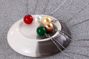 Détail de pendentifs en perles colorées sur chaînes argentées sur plateau céramique