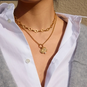 Layered gold clover necklace with portrait coin pendant worn over a white shirt