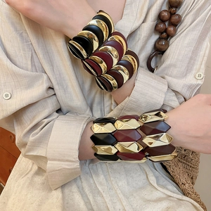 Close-up of stacked gold and resin bangles worn with a linen shirt and wooden beads