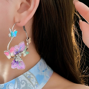 Gros plan de boucles d'oreilles créoles argentées avec papillon brodé bleu violet et strass