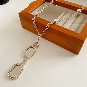 Silver-toned lorgnette glasses pendant necklace with clear crystals on a wooden box