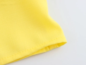 Close-up of yellow fabric texture and fine stitching detail on the shirt hemline