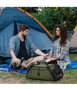 Sac de voyage vert armée posé sur l'herbe avec tente de camping en arrière-plan
