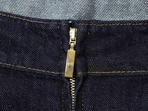Vue détaillée de la fermeture éclair dorée sur le tissu denim bleu foncé de la combinaison