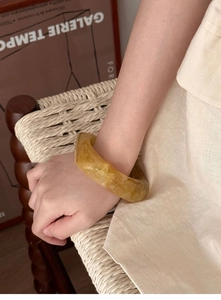 Close-up of a wide translucent amber resin bangle styled on a model's wrist in warm earth tones