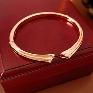 Rose gold open metal bangle on dark red wood jewelry box with polished finish