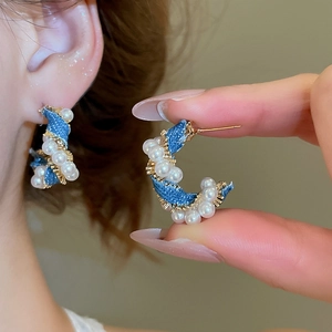 Detailed close-up of C-shaped blue denim and gold earrings with white pearl accents