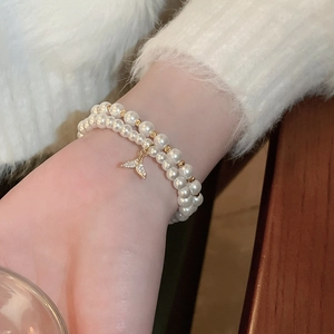 Detail of double-layer pearl bracelet with a sparkling zircon fishtail charm on a wrist