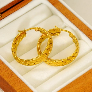 Detailed close-up of golden wheat-patterned hoop earrings on a white jewelry cushion