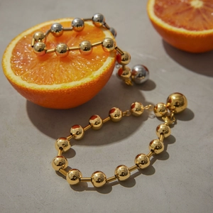 Bracelets à billes minimalistes en laiton doré et argenté sur un fruit d'orange