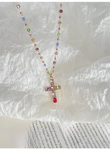 Détail macro du collier croix dorée avec cristaux colorés et chaîne perlée délicate