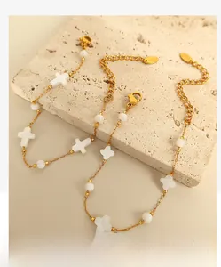 Detail of 18k gold plated chain jewelry featuring shell cross and clover pendants on stone