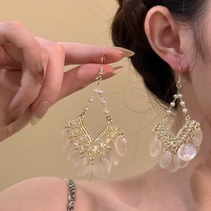 Detail of gold fringe earrings with white shell pendants and pearls on a model