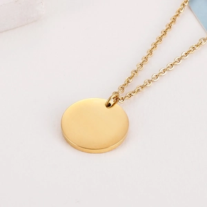 Détail macro d'un pendentif rond doré poli minimaliste sur une chaîne à maillons fine